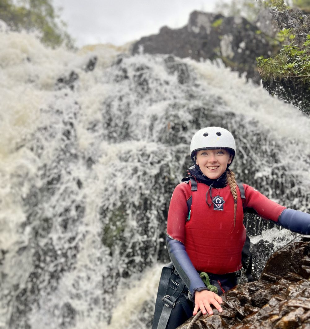 Person in helmet and gear stands beside a waterfall.