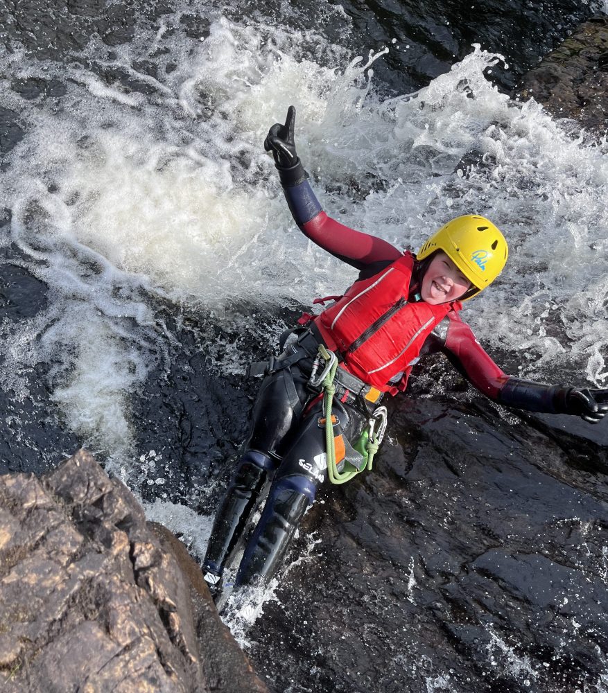 Person in helmet and life jacket sliding down rocks in a stream.