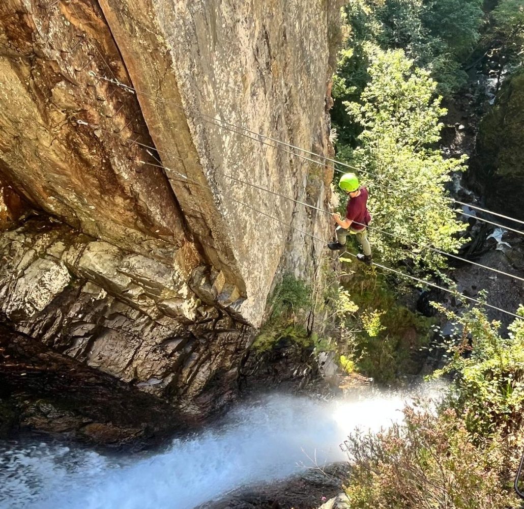 Person climbing a steep rock face near a waterfall.