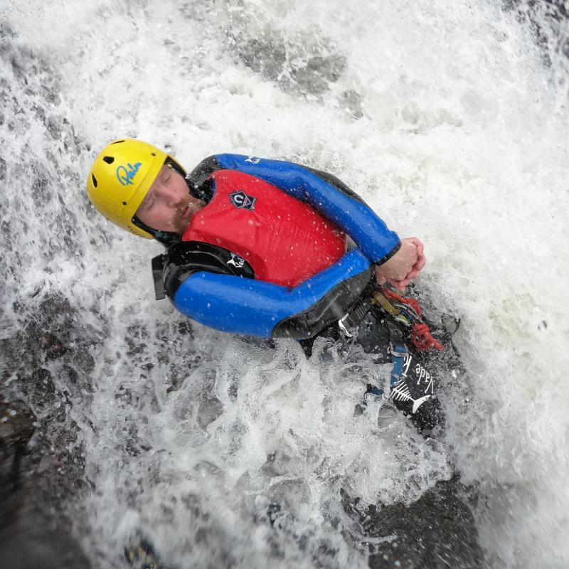Person in a red and blue wetsuit whitewater rafting, wearing a yellow helmet, surrounded by rushing water.